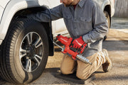 Photo of person using Craftsman cordless grease gun, SKU CMCGG001D1, to lubricate a vehicle wheel outdoors.