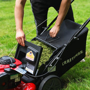 A person is removing a grass-filled bag from a CRAFTSMAN lawn mower on a grassy lawn.